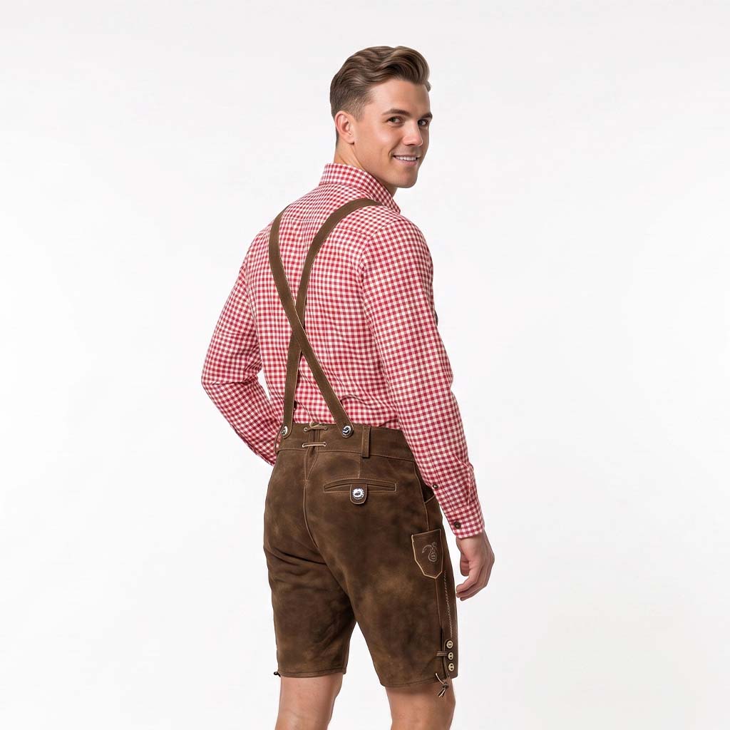 A man wearing brown leather-like lederhosen shorts with suspenders, a red and white gingham shirt, and a black tie, photographed against a plain white studio background.