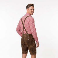 A man wearing brown leather-like lederhosen shorts with suspenders, a red and white gingham shirt, and a black tie, photographed against a plain white studio background.