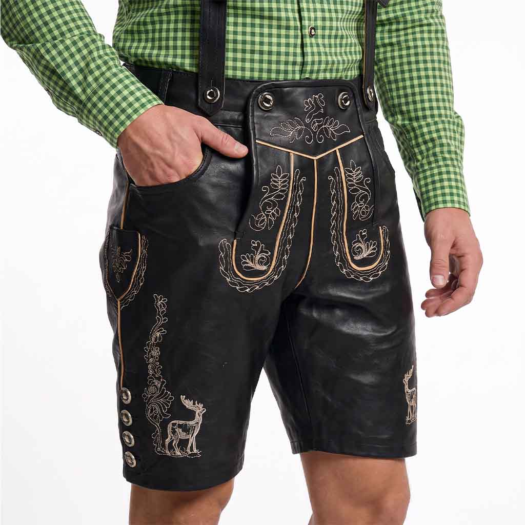 Black leather-like traditional shorts with embroidered floral and deer motifs, worn with a green gingham shirt against a white studio background.