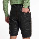 Black suede leather traditional Lederhosen shorts with lace-up waist and side buttons, worn by a model in a green gingham shirt against a white background.