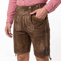Brown leather Lederhosen with white embroidery, worn by a model in a red and white check shirt against a white background.