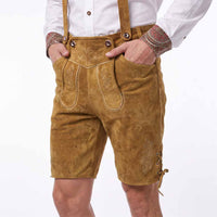 A person wearing tan suede-like lederhosen shorts with embroidered details, suspenders, and front patch pockets, paired with a white shirt against a plain white background.