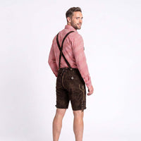 A man wearing traditional Bavarian-style dark brown leather shorts with suspenders, a red and white checkered long-sleeve shirt, and dark suspenders, photographed against a plain white studio background.
