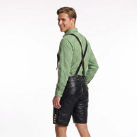 A man wearing a green and white checkered long-sleeve shirt and black leather-like suspenders over black shorts, shown from the back against a plain white studio background.