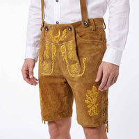 A person wearing tan suede-like traditional lederhosen shorts with yellow embroidered floral and scroll motifs, paired with a white button-up shirt, shown against a plain light background.