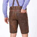Rear view of a person wearing brown leather traditional Lederhosen with suspenders, a blue and white gingham shirt, and bare legs against a white studio background.