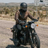 A rider wearing a RIDERACT brown leather motorcycle jacket while riding a motorcycle