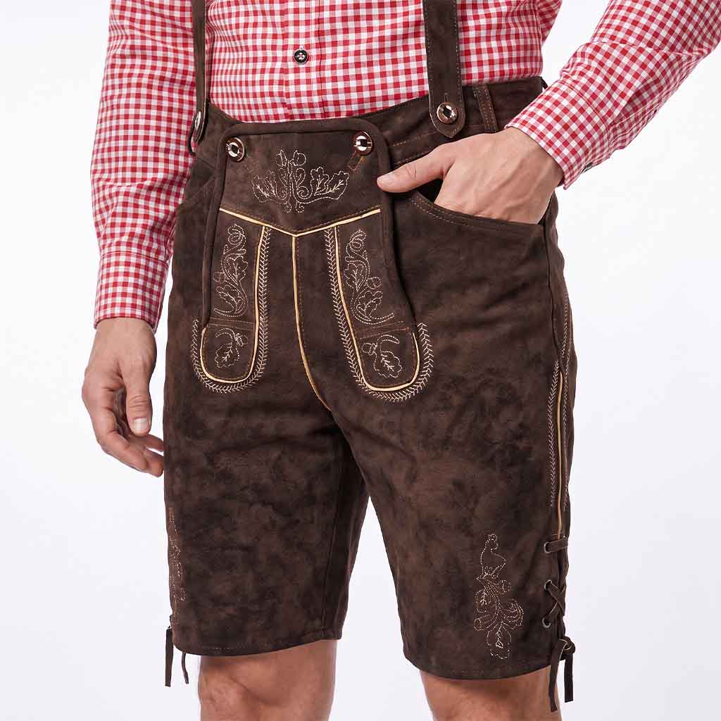 A person wearing dark brown suede lederhosen with embroidered details and suspenders, paired with a red and white gingham shirt, shown from the waist down against a white background.